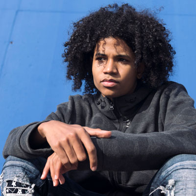 A boy sitting in the sun deep in thought.