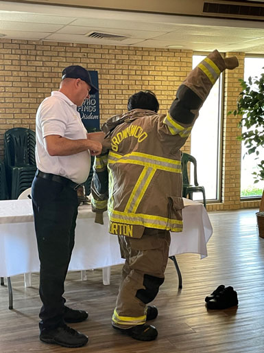A recruiter from the local fire department helps a youth try on a fireman's suit.
