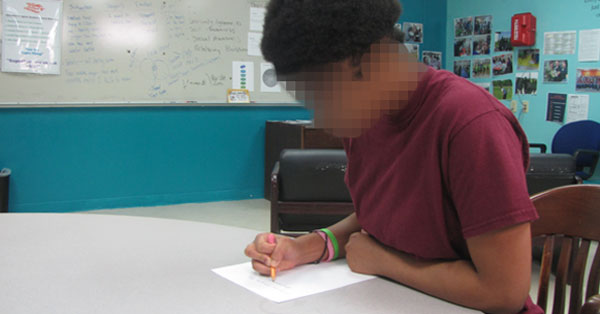 Photo of a youth writing at a table.