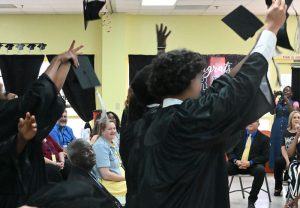 Youth toss their caps in the air to celebrate at the Mart graduation ceremony.